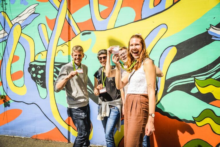 Gruppe von vier Personen mit Teamkit-Umhängebändern posiert fröhlich vor einem Graffiti